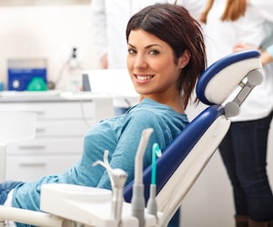 Young woman with dark hair sitting in a blue dental chair wearing a blue top